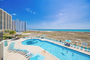 Ein Schwimmbad mit Liegestühlen, Blick auf den Strand und einem Hotelgebäude.