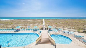 Un espace piscine comprenant plusieurs piscines, une allée centrale et une vue sur la plage.