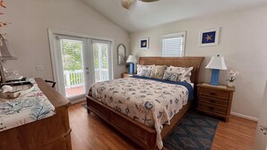 A bedroom with a wooden bed, a ceiling fan, a nightstand with a lamp, a dresser, and a window with blinds.