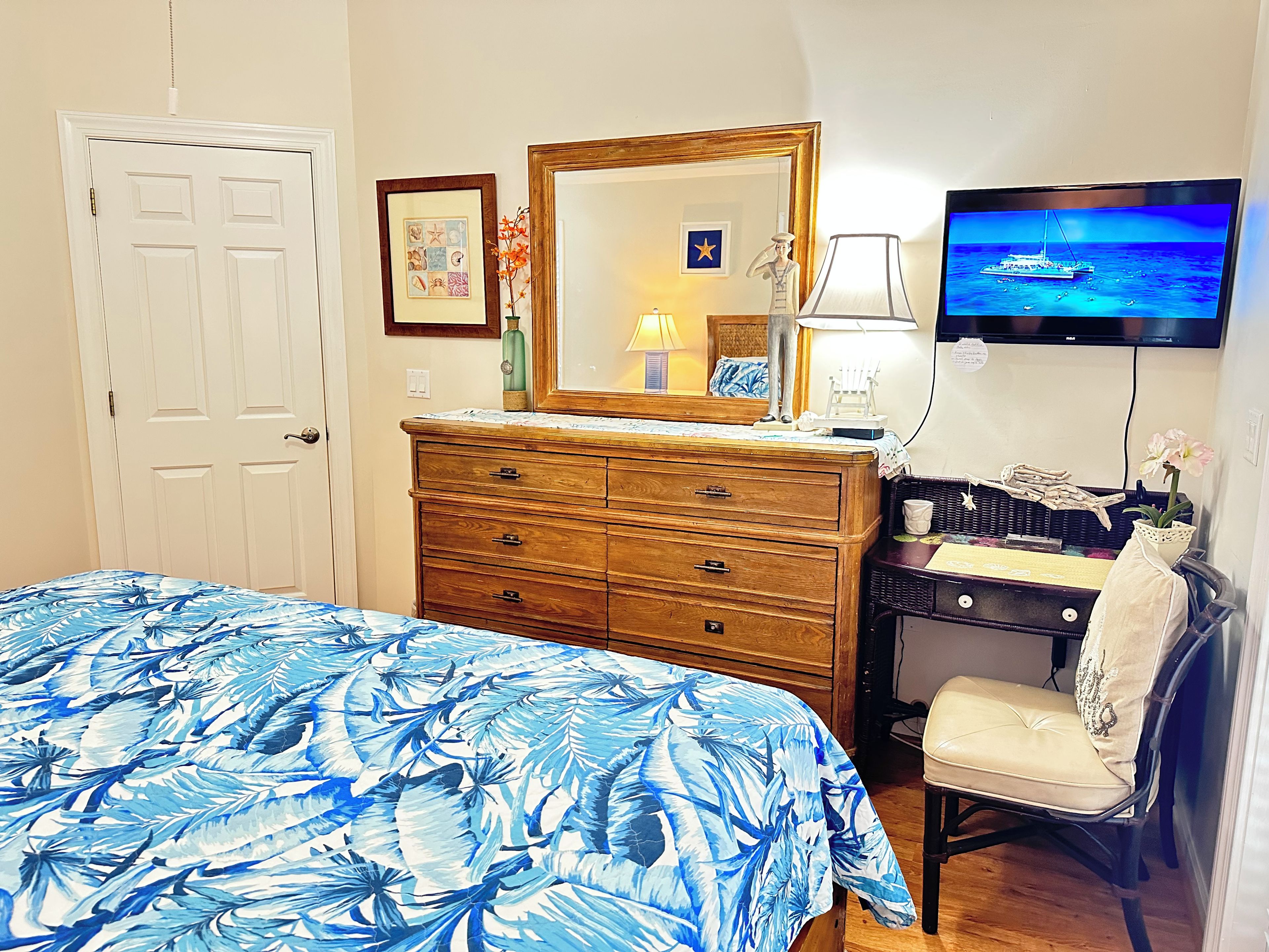 Un dormitorio con cama, cómoda, silla, televisor y espejo en la pared.