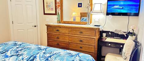 Un dormitorio con cama, cómoda, silla, televisor y espejo en la pared.