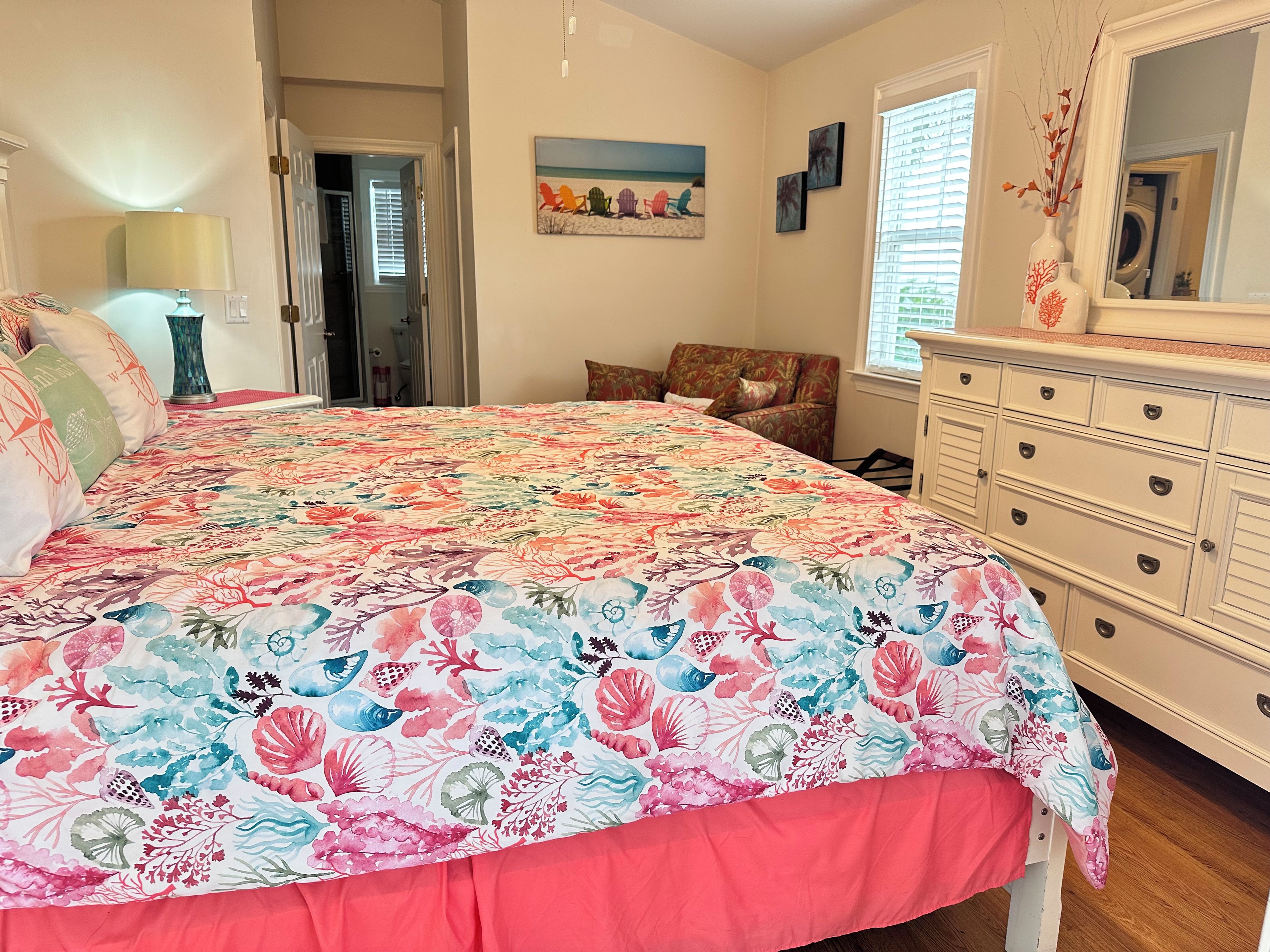 A bedroom with a large bed, a dresser, a chair, and a painting on the wall.