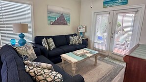 A living room with a dark-colored sofa, a coffee table, a ceiling fan, and a painting on the wall.