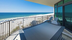 A balcony with a view of the beach, a table, and two chairs.