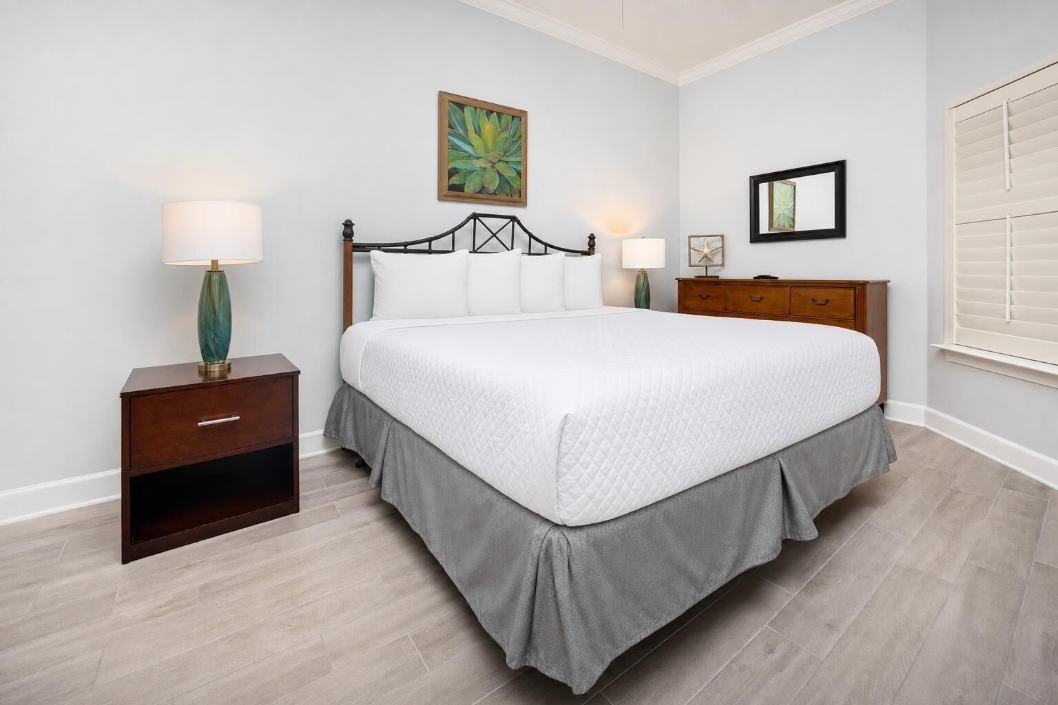 A bedroom with a bed, nightstands, a dresser, a painting, and a window with blinds.