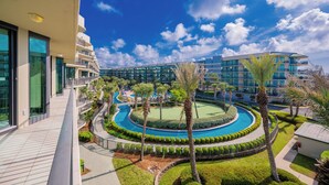 Een modern hotel met een zwembad, weelderige beplanting en een helderblauwe lucht.