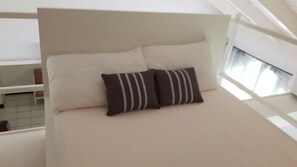 A bed with a white headboard, two pillows, and a light-colored mattress in a room with a window and a white railing. - Coral Keys at Sandcastles (Ocho Rios)