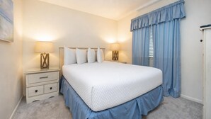 A bedroom with a large bed, two bedside tables, a nightstand, a window with curtains, and a door.