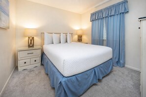 A bedroom with a large bed, two bedside tables, a nightstand, a window with curtains, and a door.
