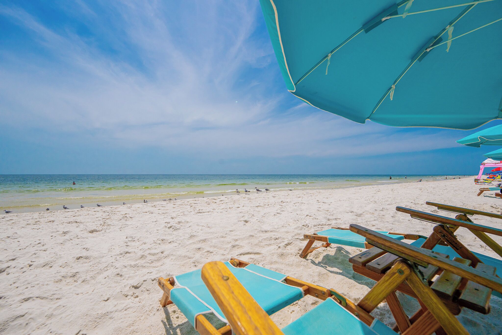 A beach with clear skies, a sandy shore, and wooden lounge chairs.