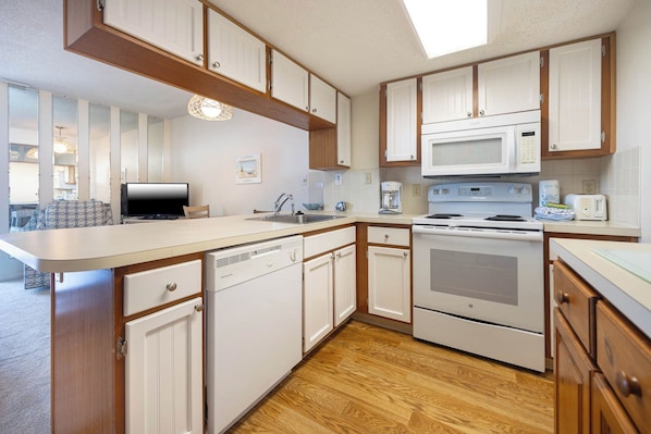 A compact kitchen with white cabinets, a microwave, an oven, and a dishwasher.