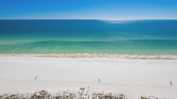 A beach with clear turquoise water, a sandy shore, and a few people in the distance.