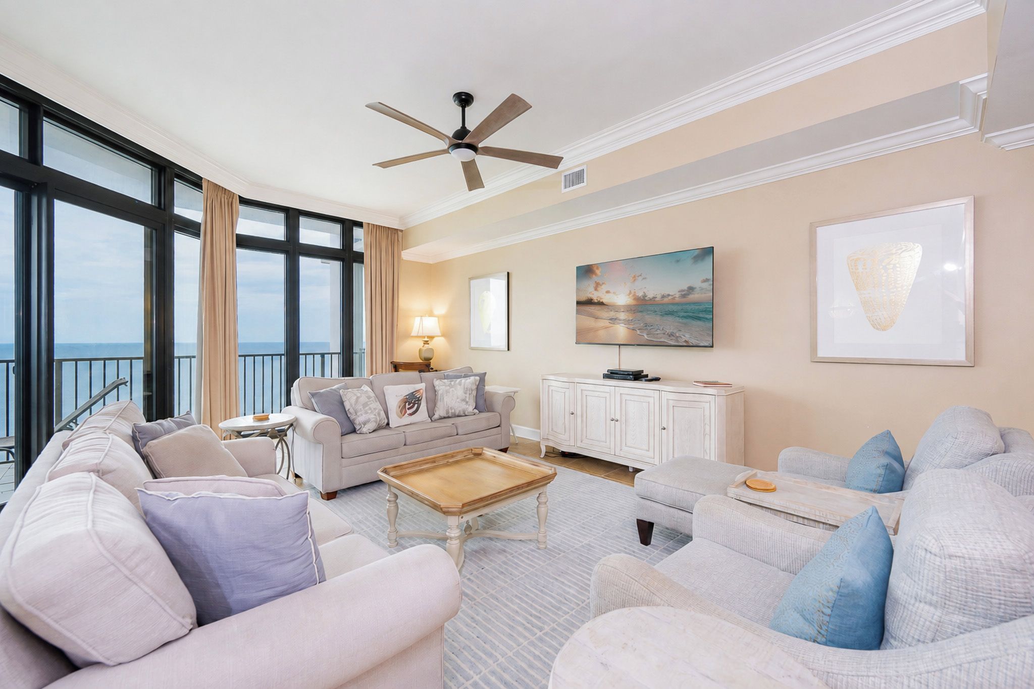 A spacious living room with a large window, a ceiling fan, and a view of the ocean.