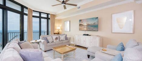 A spacious living room with a large window, a ceiling fan, and a view of the ocean.