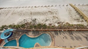 Zona de piscina con tobogán, sillas de descanso y un muelle de madera con vistas a la playa.