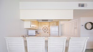 A kitchen with white cabinets, a white refrigerator, a microwave, and a table with four white chairs.