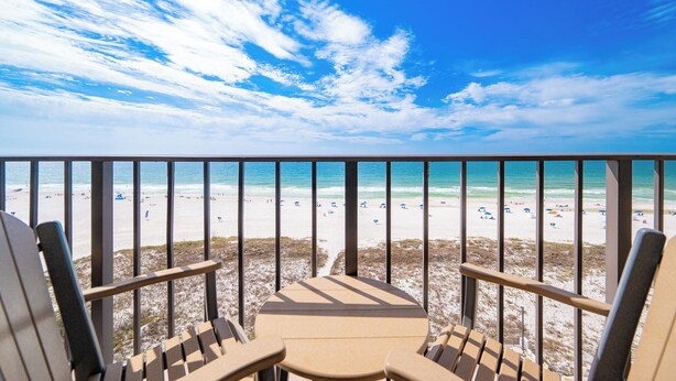 A balcony with a view of a beach, featuring a table and chairs.