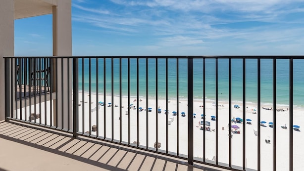 A balcony with a view of a beach with umbrellas and people. - Ocean Breeze Escape Phoenix X 1012 (Orange Beach)