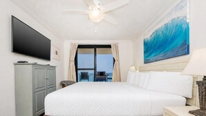 A hotel room with a bed, a flat-screen TV, a ceiling fan, a painting, and a view of the balcony. - Ocean Breeze Escape Phoenix X 1012 (Orange Beach)