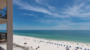 A beach view from a balcony with white sand, clear blue water, and a few umbrellas. - Ocean Breeze Escape Phoenix X 1012 (Orange Beach)