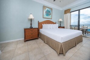 A hotel room with a large bed, two bedside tables with lamps, a painting on the wall, and a balcony with a view. - ~ Premium 2BR @ Phoenix V (Orange Beach)
