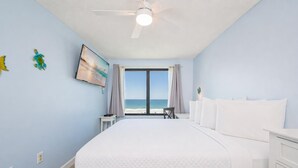 A bedroom with a bed, a nightstand, a chair, a ceiling fan, and a view of the ocean.