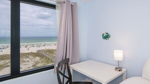 A room with a view of the beach, a white table, a chair, and a lamp.