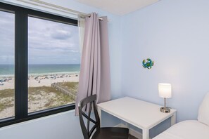 A room with a view of the beach, a white table, a chair, and a lamp.