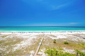 A beach with a wooden boardwalk leading to the shore, white sand, and a clear blue sky.