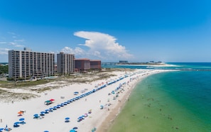 Resort à beira-mar com vários edifícios altos, uma extensa faixa de areia com guarda-sóis e águas turquesa cristalinas.