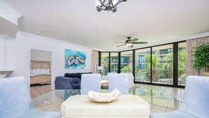 A modern living room with a glass coffee table, a sofa, and a ceiling fan. - Spend Vacation on the Bay!! 3 BR 3 BA ~ LOW FLOOR! (Orange Beach)