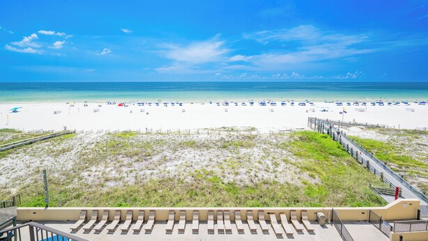 A beach with a wooden walkway leading to the shore, white sand, and clear blue sky.