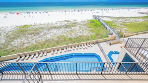 A beach view from a balcony with a pool and lounge chairs.