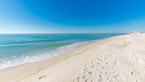 A beach with a clear sky, calm sea, and footprints in the sand.