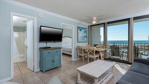Una habitación con televisión, una mesa de madera, un sofá y un balcón con vista al mar.