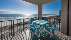 Un balcon avec une table et des chaises, donnant sur une plage et l’océan.