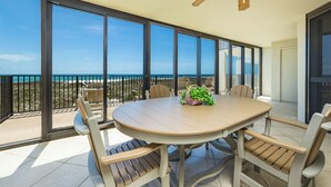 Un balcon avec une table ronde et des chaises, une vue sur l’océan et un ventilateur de plafond.