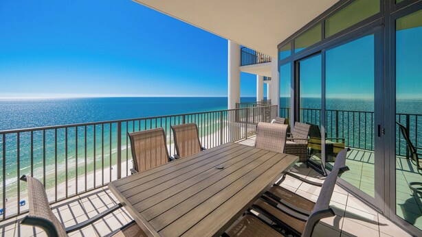 A balcony with a wooden table and chairs, overlooking a beach and the ocean. - The Oasis at Orange Beach, formerly known as Phoenix West II, Unit 1710 (Orange Beach)