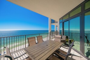 Un balcon avec une table et des chaises en bois, donnant sur une plage et l’océan.
