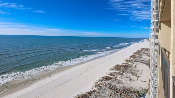 A beach view from a balcony with a clear sky, sandy beach, and ocean.