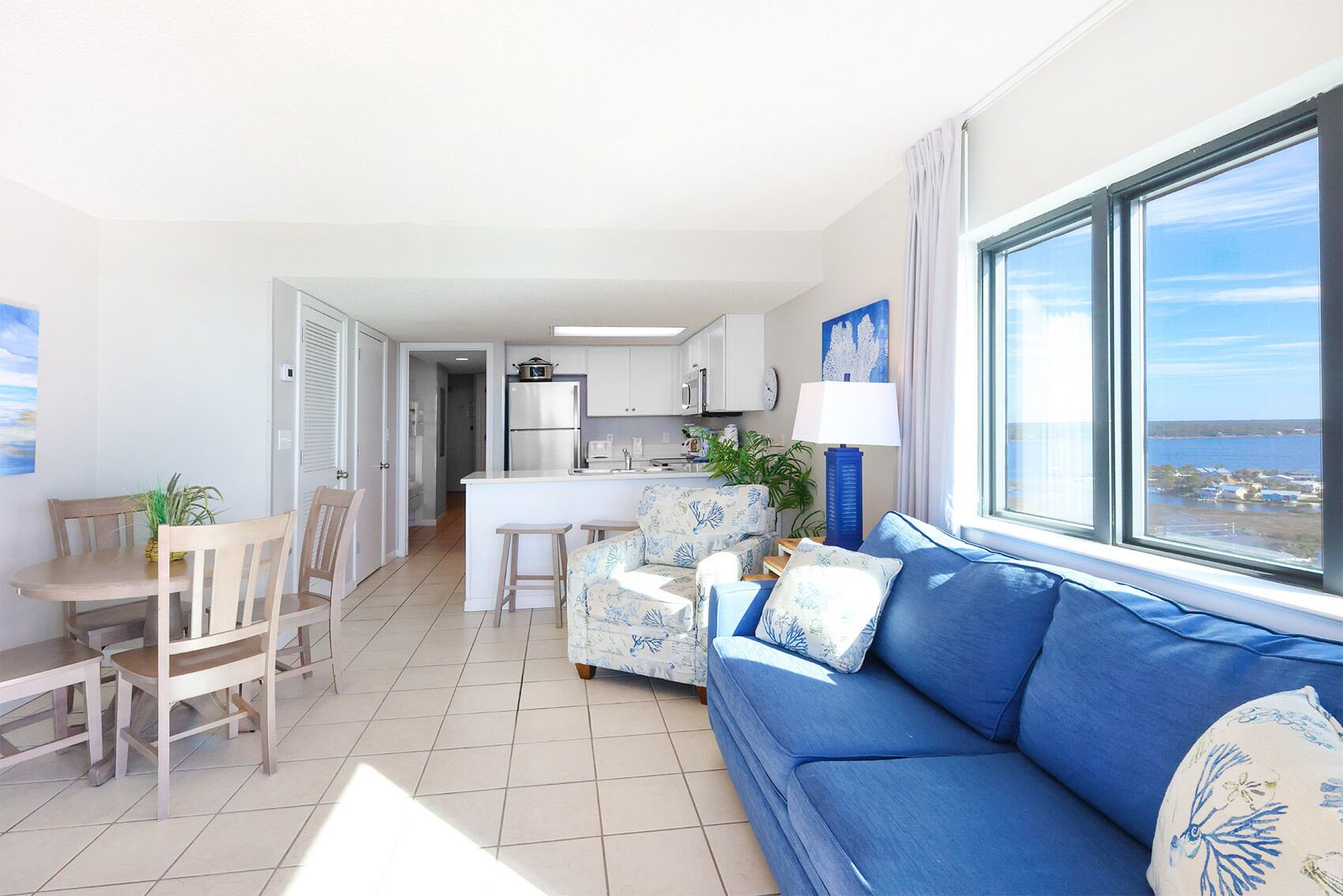 Een moderne woonkamer met een blauwe bank, een eethoek met houten stoelen, en een keuken met witte kasten.
