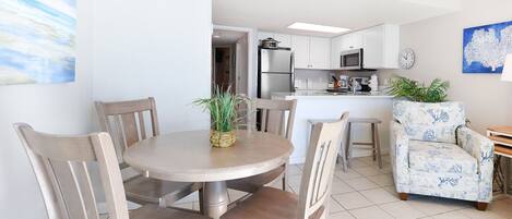 Una cocina moderna con armarios blancos, una isla central y un comedor con sillas de madera y una mesa redonda.