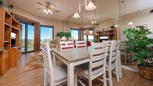 A spacious dining area with a wooden table and chairs, a large mirror, and a view of the outdoors through a sliding glass door.