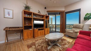 A living room with a large TV, wooden entertainment unit, red sofa, and a balcony with a view.