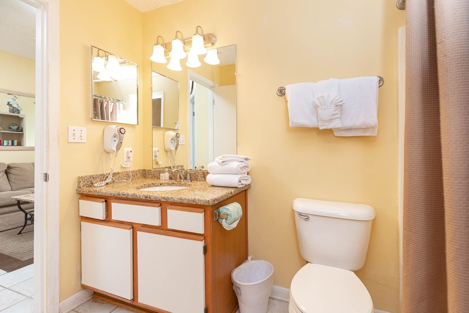 A bathroom with a granite countertop, a white toilet, and a towel rack with folded towels.