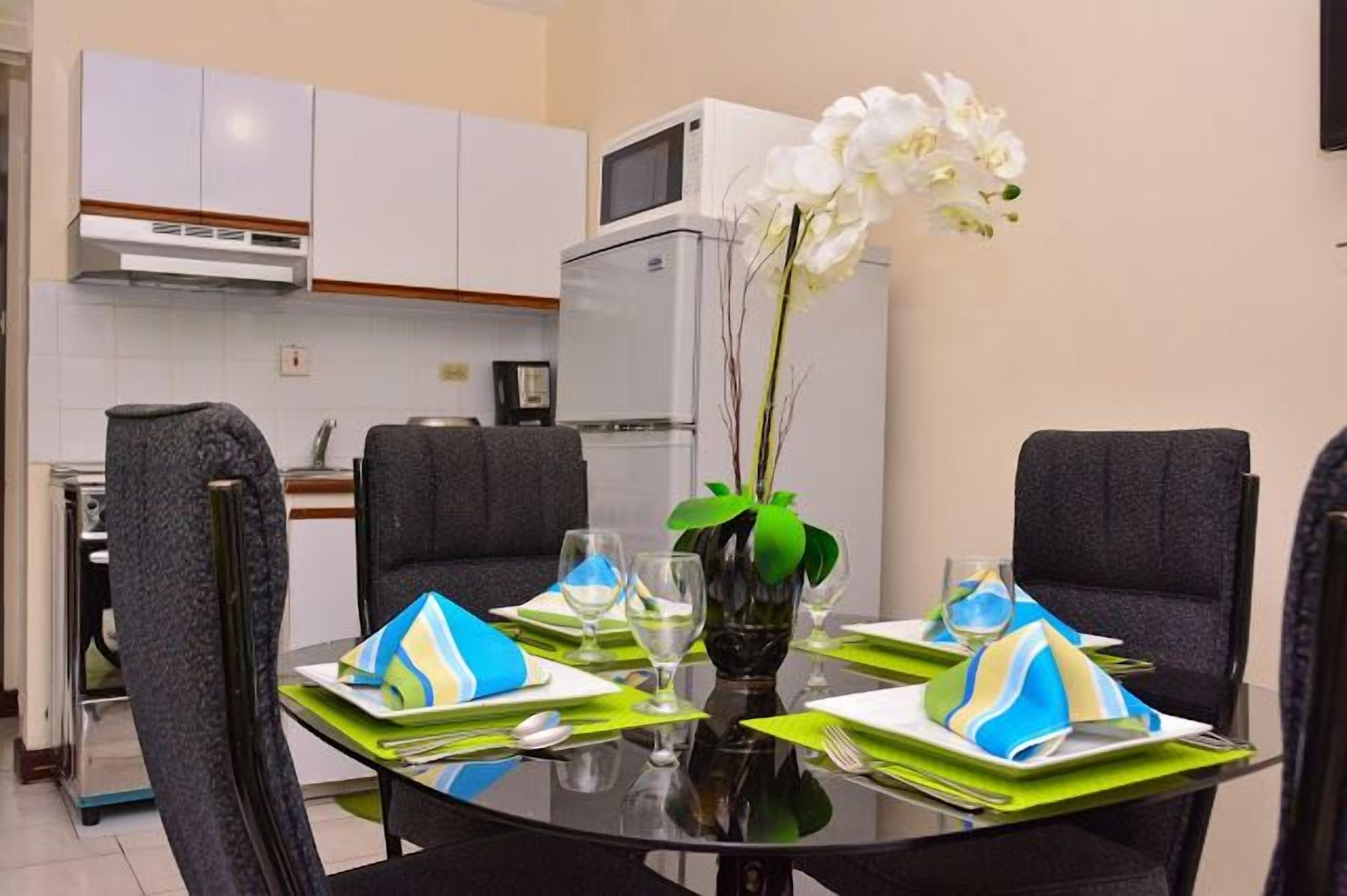 A dining area with a round table set for four, a microwave, and a refrigerator in the background.