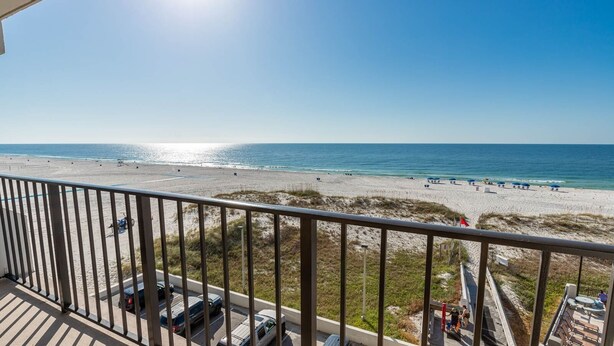 A beach view from a balcony with a railing, beach umbrellas, and people. - Island Winds East Condo 404 *BeachFront* (Gulf Shores)