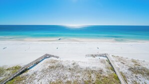 Ein Strand mit einem hölzernen Steg, der zum Wasser führt, Sanddünen und einem strahlend blauen Himmel.