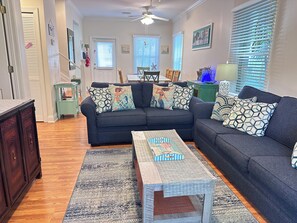 A living room with a dark sofa, patterned cushions, a coffee table, and a wooden floor.