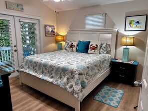 Une chambre à coucher comprenant un lit, des tables de chevet, une commode, une fenêtre avec des stores et une porte.